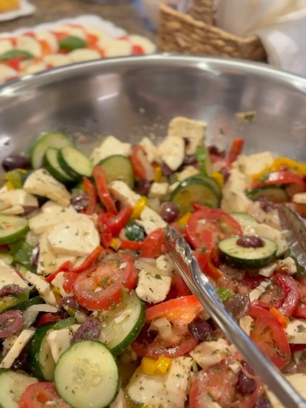 Bowl of salad with fresh mozzarella, tomatoes, cucumbers, peppers, and olives at a catered party