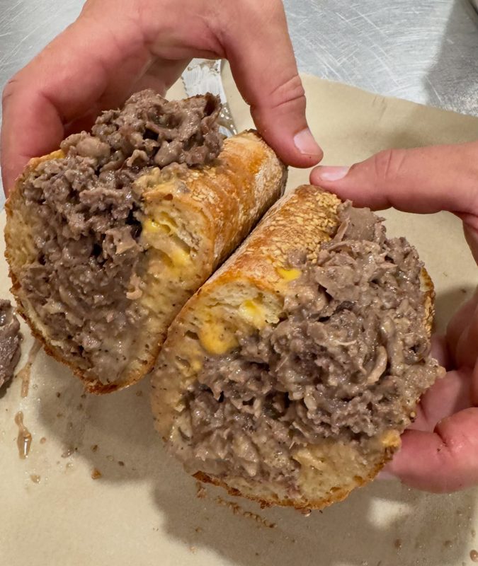 Cheesesteak on a homemade roll, cut in half showing steak, melted cheese, and gravy