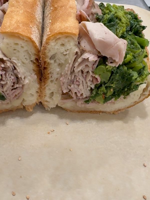 Sliced roast pork sandwich on a homemade loaf with sharp provolone and broccoli rabe