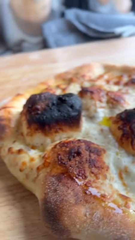 Video still of a white pizza with a blistered, charred crust on a wooden board